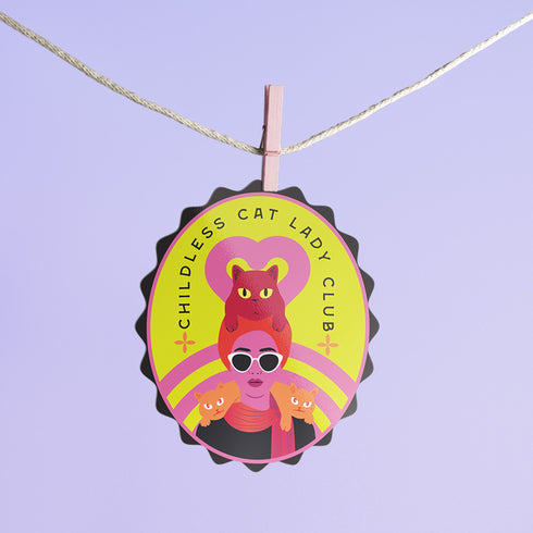 Vibrant oval sticker reading "Childless Cat Lady Club". Features cartoon woman with sunglasses surrounded by cats. Bold retro design in pink, yellow, and red.